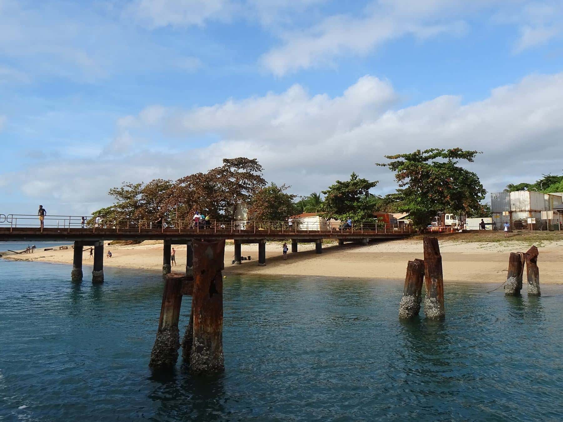 An old timber jetty with weathered pylons reaching out into clear water at Seisia